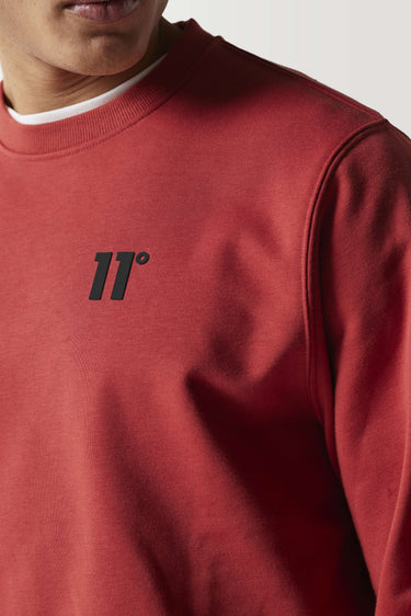 Red crewneck sweatshirt close-up with black chest logo and ribbed collar