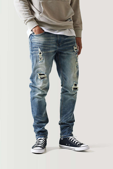 Mid-blue ripped jeans with multiple distressed patches and frayed cuffs