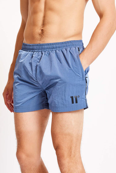 Close-up of blue swim shorts: elastic waistband and side taping with logo on leg.