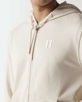 Light beige full-zip hoodie close-up with drawstring hood and chest logo