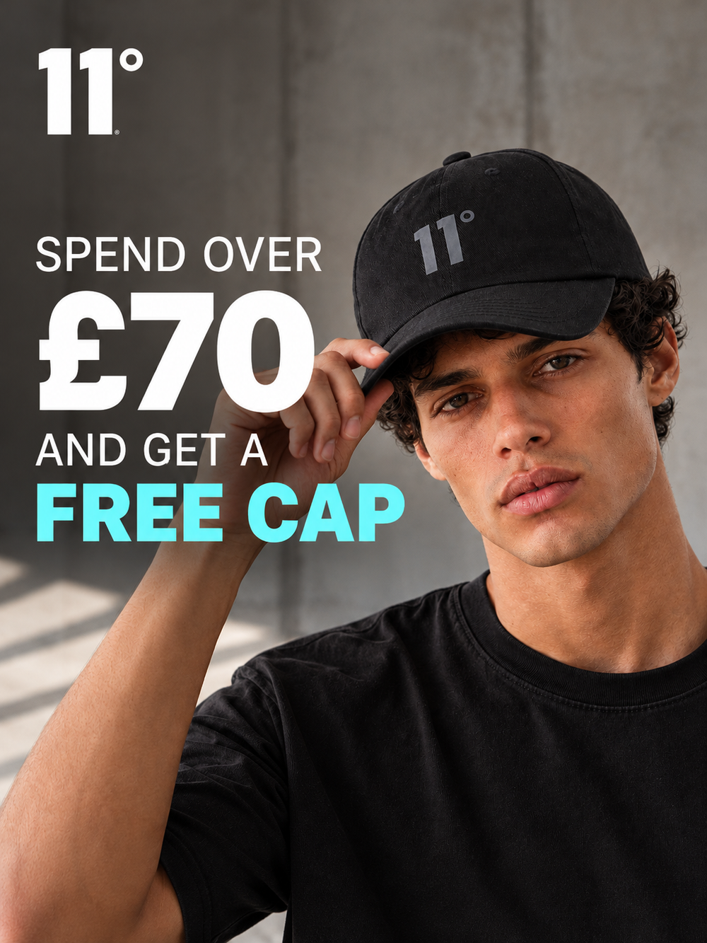 A man wearing a black 11° cap and black t-shirt, holding the brim of the cap. Large promotional text on the left reads '11° SPEND OVER £70 AND GET A FREE CAP'.