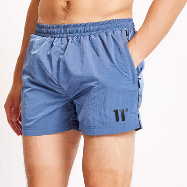 Close-up of blue swim shorts: elastic waistband and side taping with logo on leg.